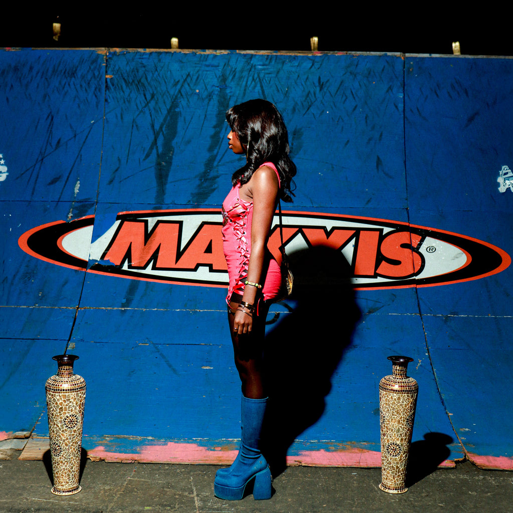 Woman in a pink top and black stockings standing in front of a Maxxis wall.